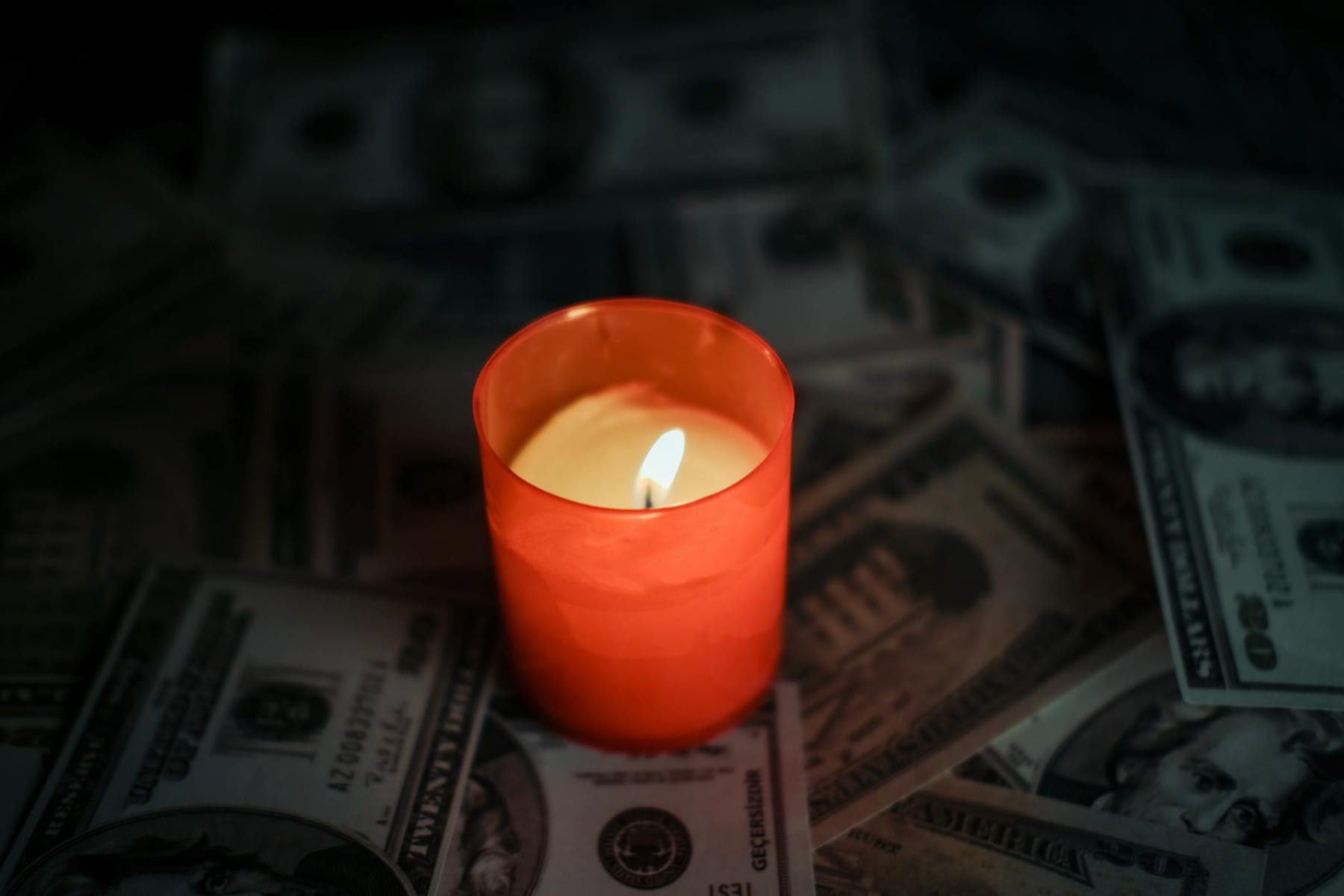 A red candle glowing among scattered US dollar banknotes, creating a dramatic ambiance. on The Manifesting Light