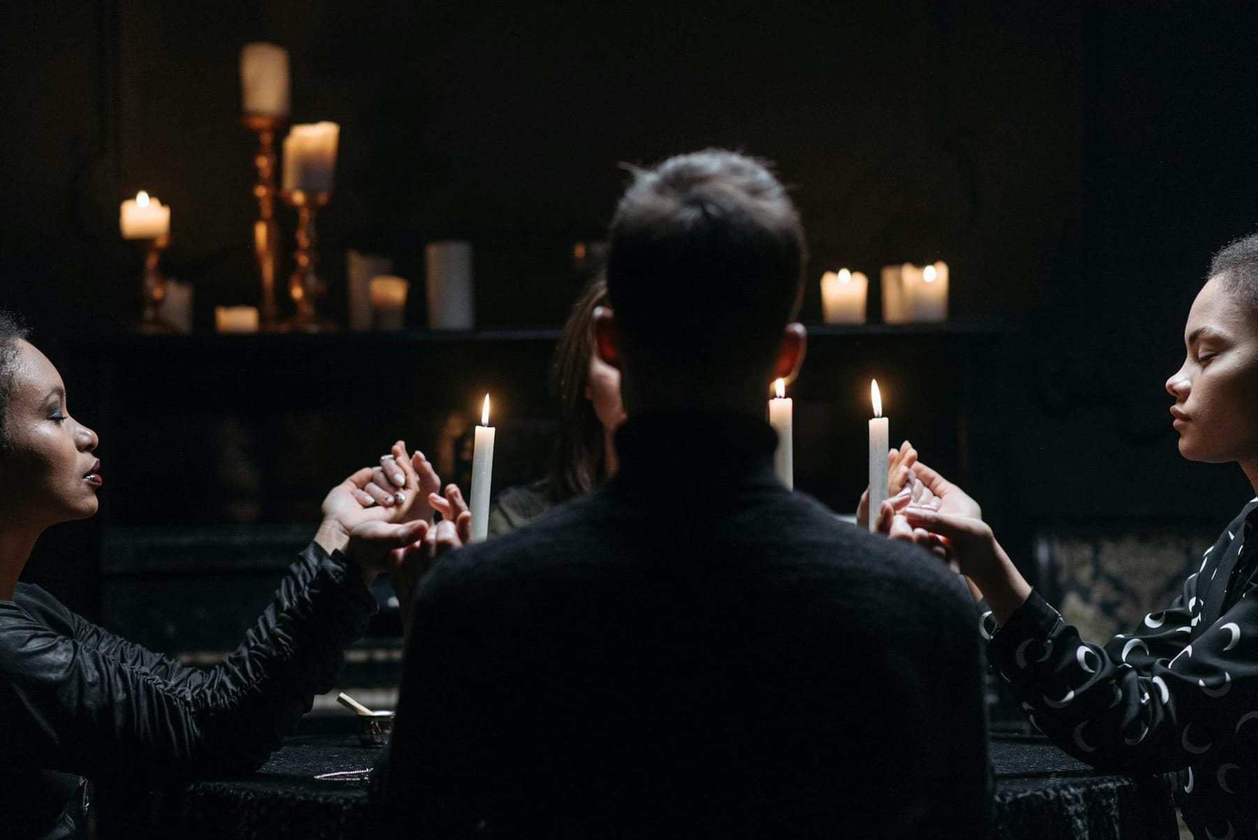 A group of women holding hands in a candlelit mystical seance session indoors. on The Manifesting Light