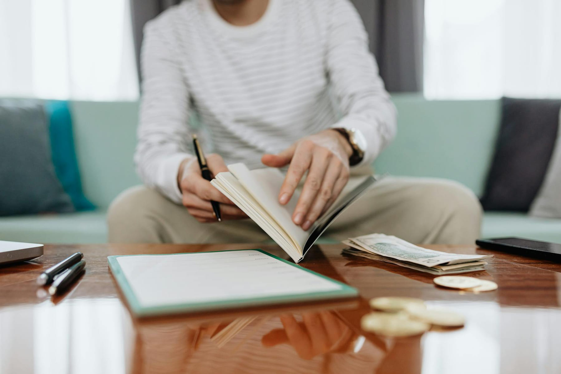 Individual reviewing finances at a table with notebook, money, and laptop. on The Manifesting Light