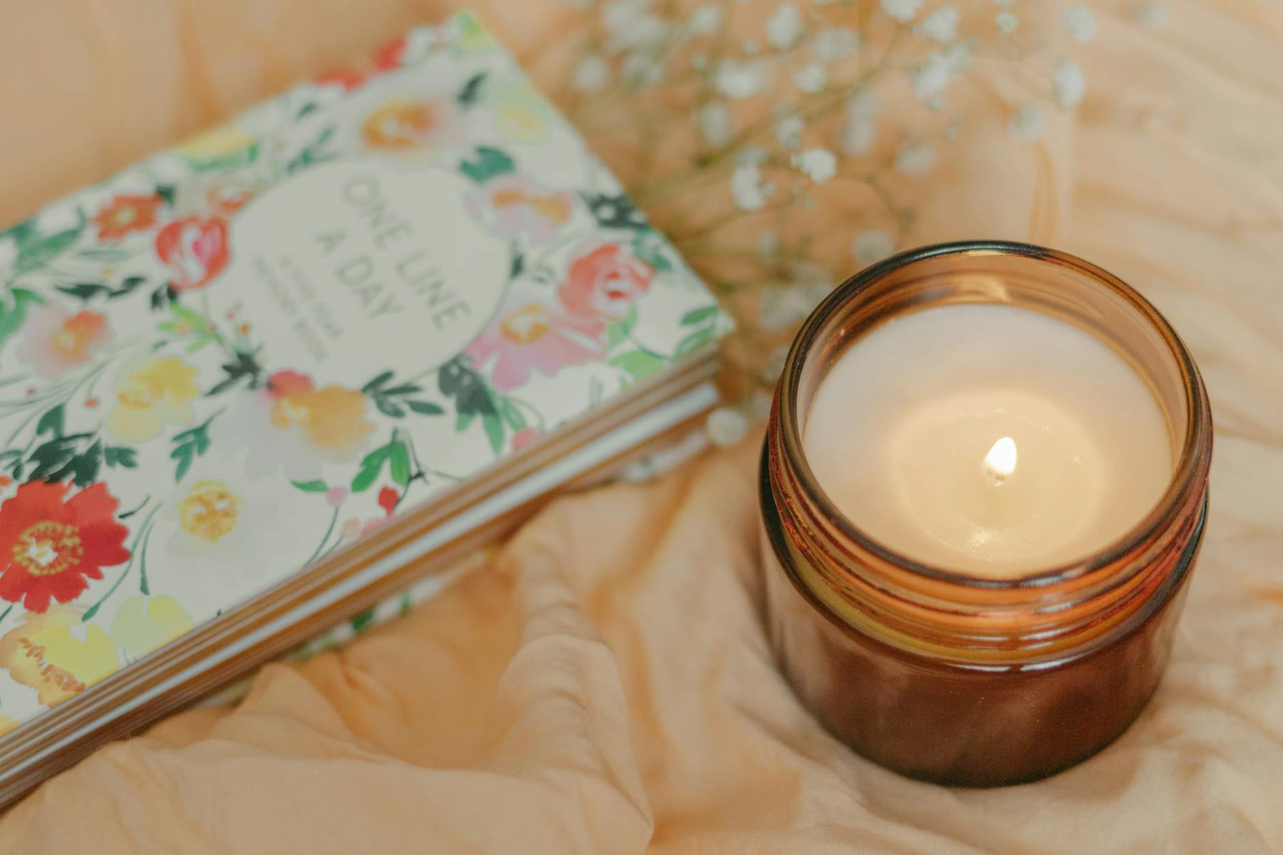 Floral journal and warm candle on soft fabric, creating a cozy atmosphere. on The Manifesting Light