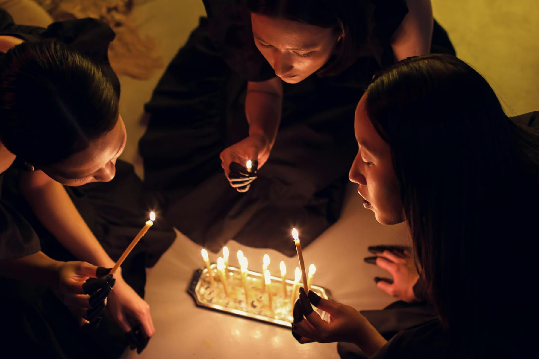 Top view of women holding candles in a dimly lit ritual setting, evoking spiritual themes. on The Manifesting Light