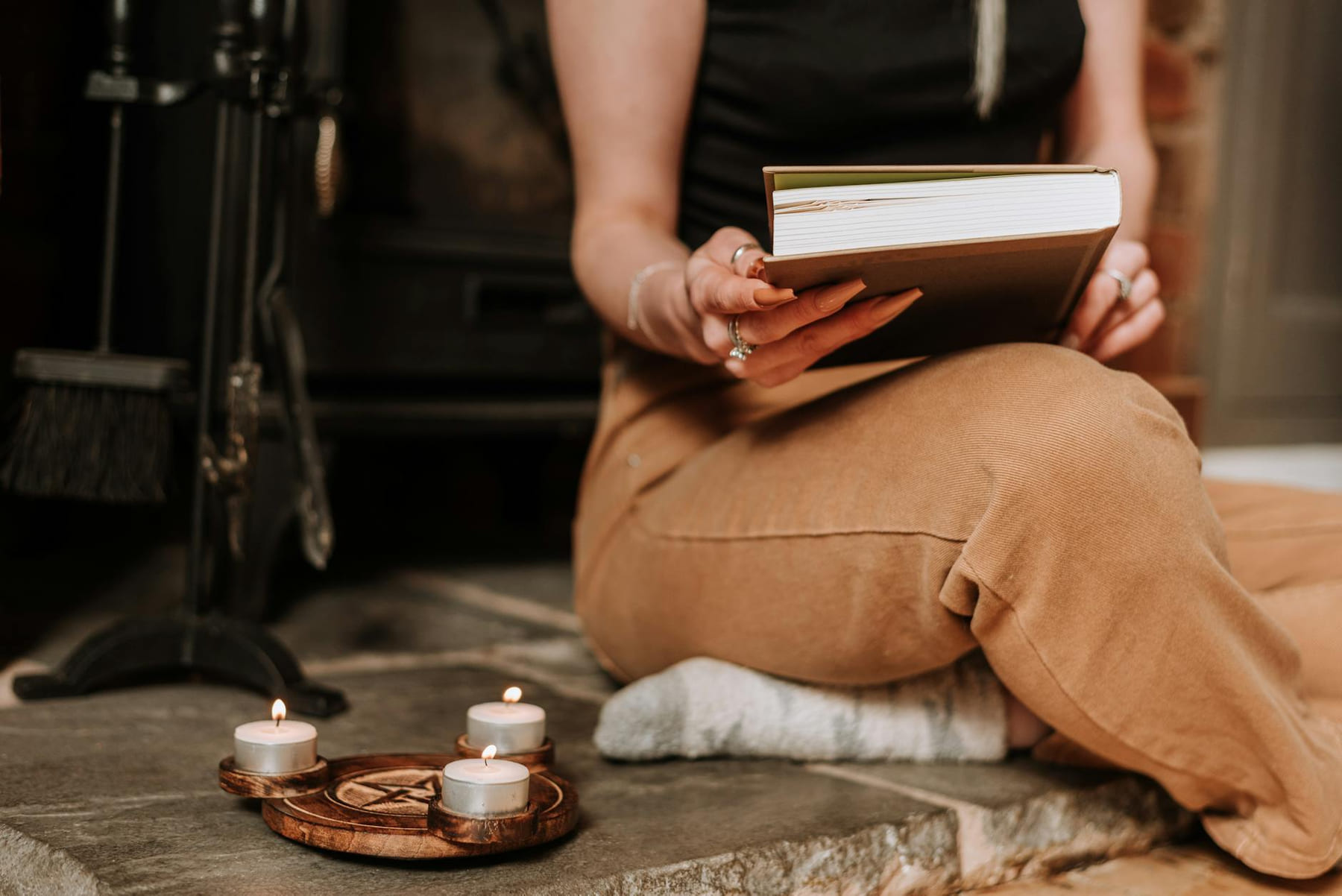 Crop anonymous female with book in hands near pentagram candle holder on floor on The Manifesting Light