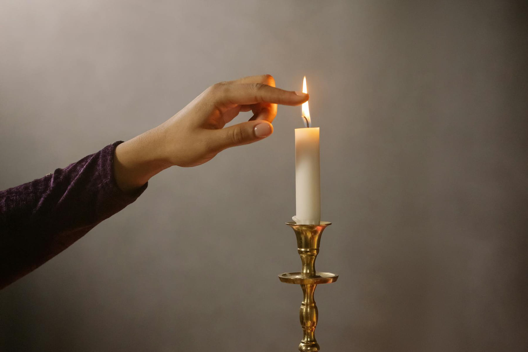 A hand gently lights a single candle flame on a brass holder, creating a serene atmosphere. on The Manifesting Light