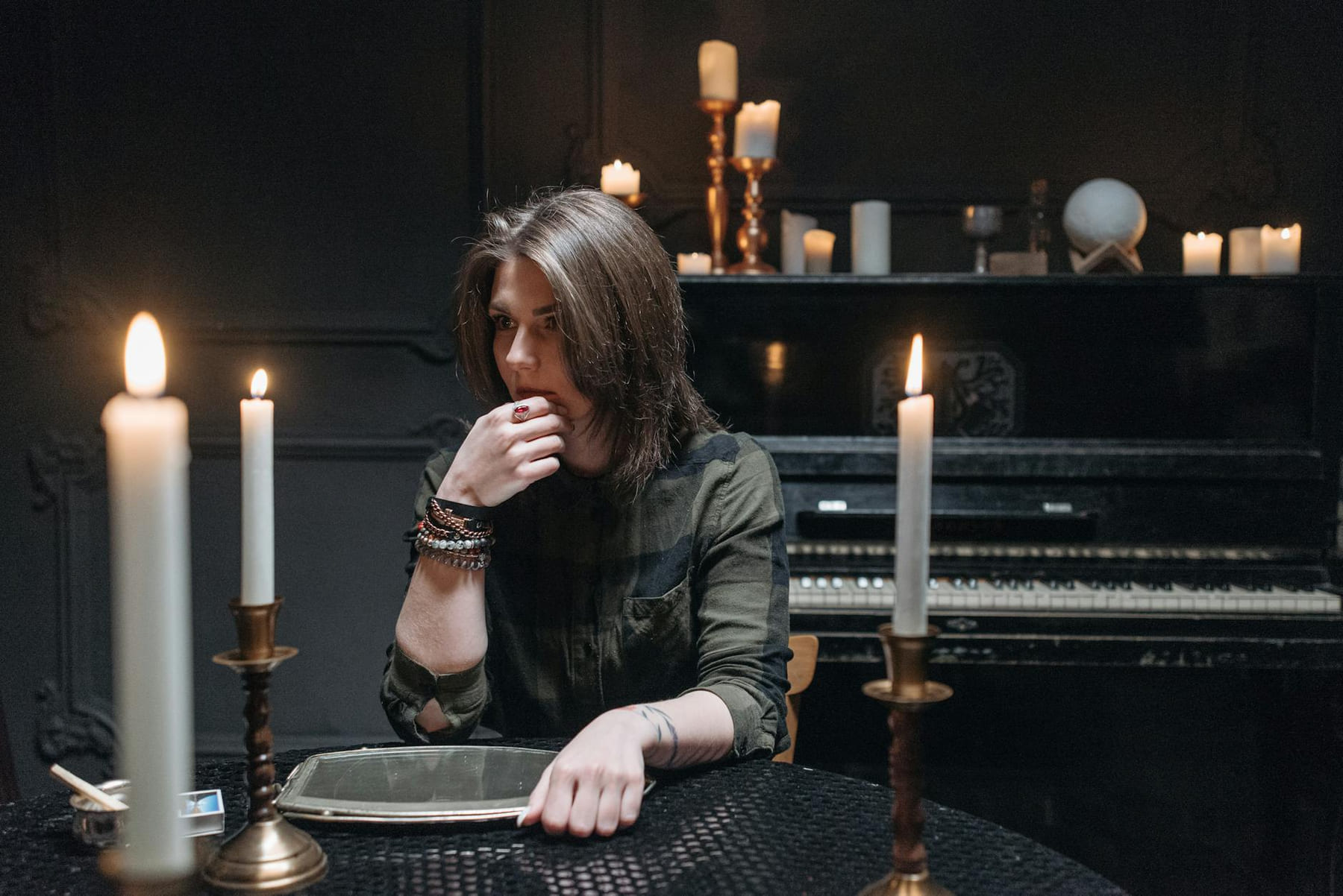A thoughtful woman sits at a dark table with candles, evoking a mystical ambiance. on The Manifesting Light