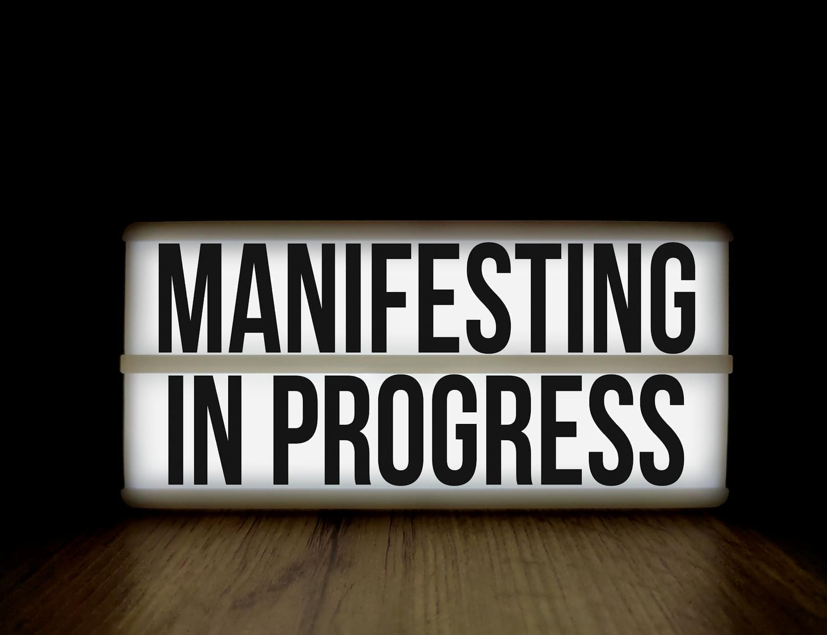 Illuminated lightbox sign with the motivational message 'Manifesting in Progress'. on The Manifesting Light
