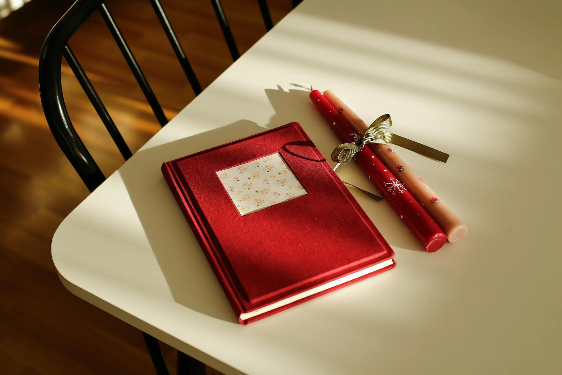 Elegant red journal and two decorative candles on a sunlit table, creating a warm ambiance. on The Manifesting Light