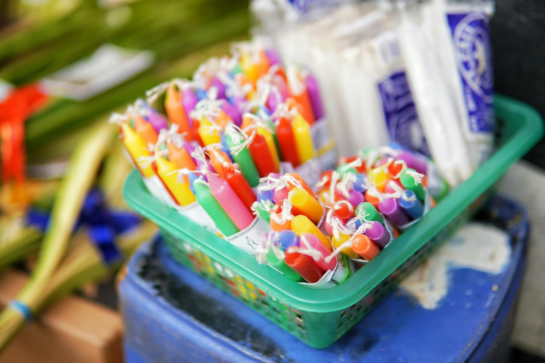 Vibrant multi-colored candles arranged in a green basket for sale outdoors. on The Manifesting Light